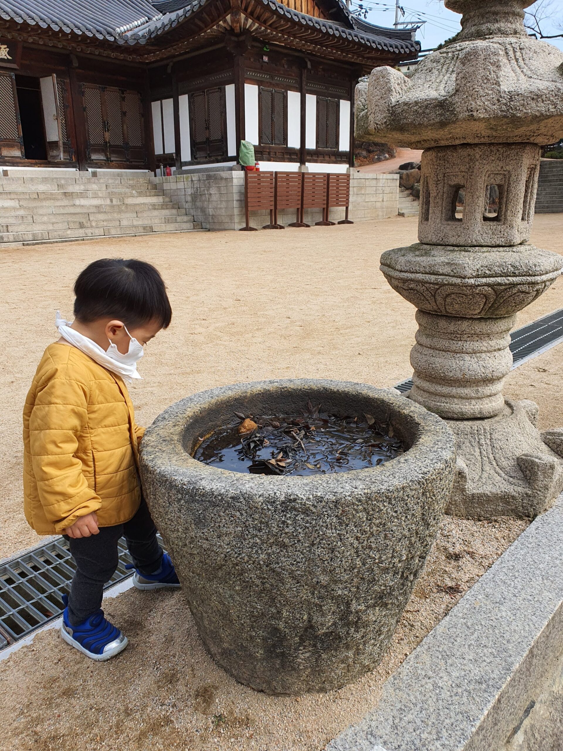 A child looking into a stone water basin beside a stone lantern at Gilsangsa temple